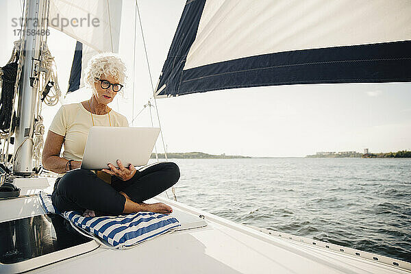 Ältere Frau arbeitet aus der Ferne beim Segeln Boot auf sonnigen Tag