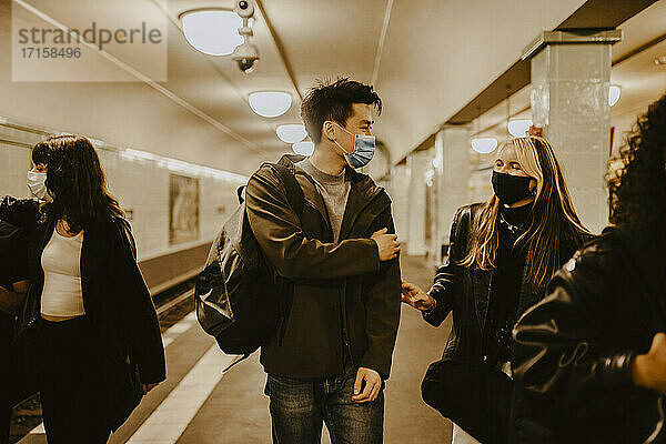 Männliche und weibliche Freunde unterhalten sich in einer beleuchteten U-Bahn-Station während COVID-19