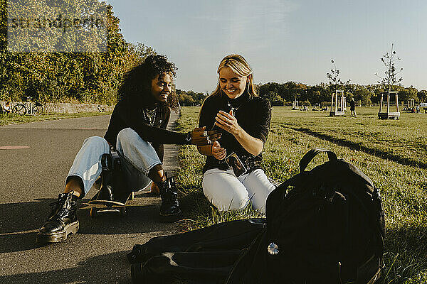 Lächelnde weibliche Freunde mit Smartphone sitzen im Park