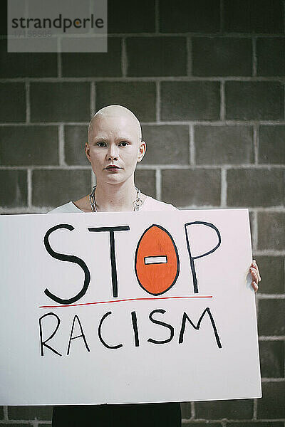 Junge Demonstrantin mit Stop-Rassismus-Schild an der Wand