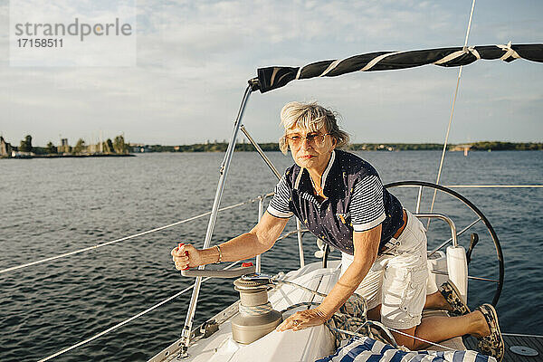 Ältere Frau dreht Griff beim Segeln Boot im Meer am sonnigen Tag