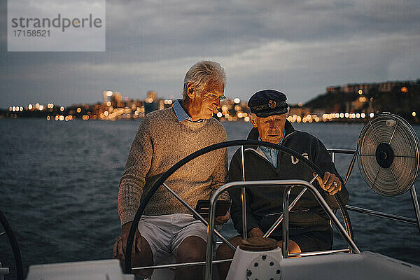 Senior Mann führt männlichen Freund beim Segeln Boot während des Sonnenuntergangs