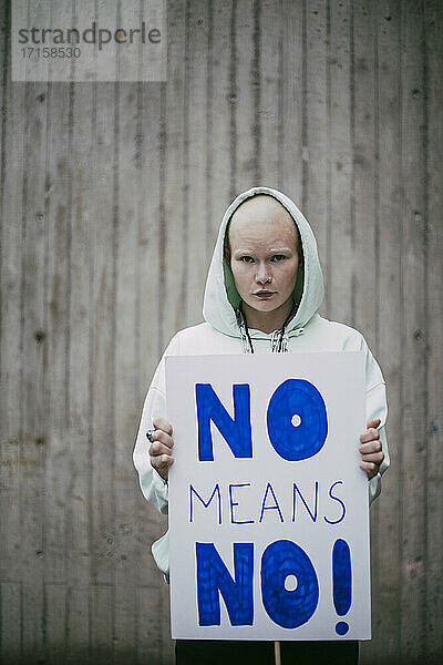 Porträt einer weiblichen Aktivistin  die ein No means no -Plakat an die Wand hält