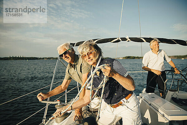Älterer Mann dreht Griff auf Boot  während Freundin mit Seil gegen den Himmel steht