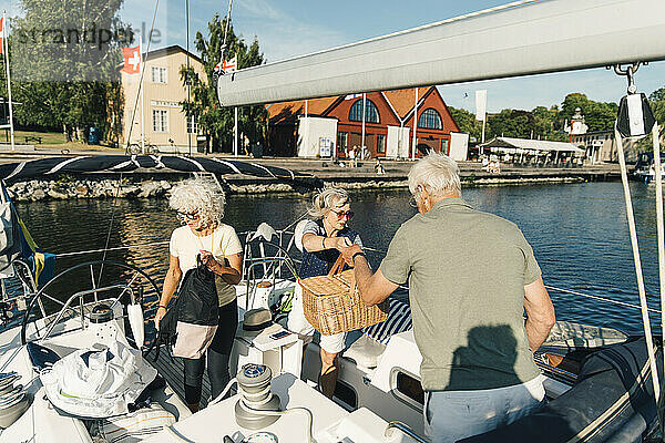 Weibliche und männliche Freunde mit Picknick Dinge in Segelboot auf sonnigen Tag