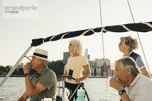 Männliche und weibliche Freunde schauen beim Segeln im Boot an einem sonnigen Tag weg
