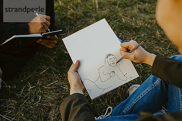 Ausgeschnittenes Bild von Männerhänden  die in einem Buch im Park skizzieren