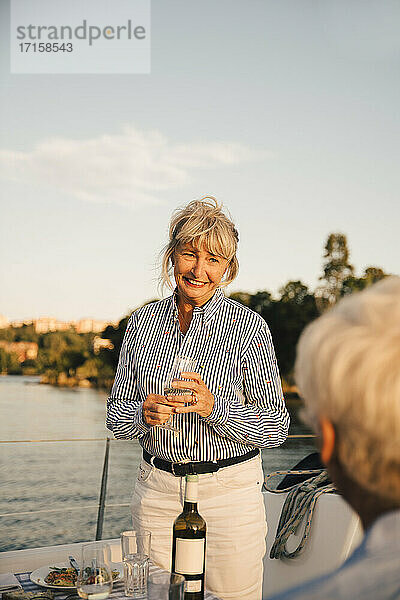 Lächelnde ältere Frau mit Weinglas schaut auf Mann in Boot gegen Himmel