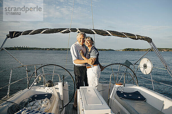 Porträt von lächelnden Senior Paar umarmt einander in Boot gegen Meer und Himmel