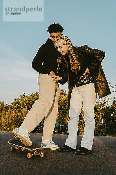 Männliche und weibliche Freunde stehen durch Skateboard im Park während des Sonnenuntergangs