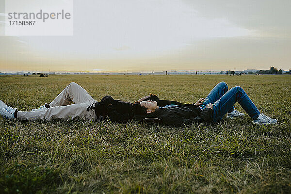 Männliche Freunde liegen auf Gras im Park während des Sonnenuntergangs