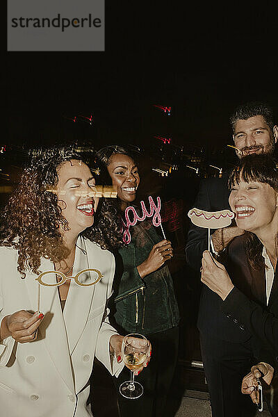 Fröhliche weibliche und männliche Kollegen lachen mit Requisiten während einer Party