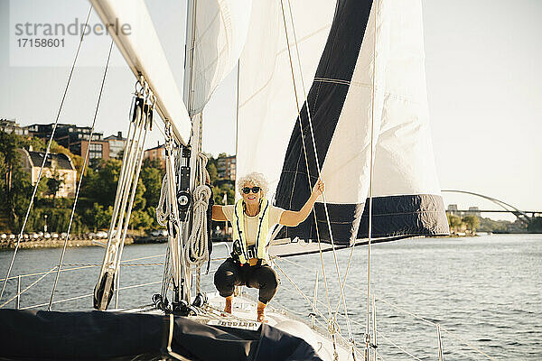 Ältere Frau hockt  während sie ein Seil im Boot an einem sonnigen Tag hält