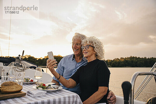 Lächelnde ältere Paar unter Selfie durch Smartphone gegen Himmel während Sonnenuntergang