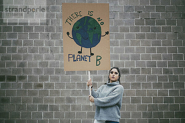 Junge weibliche Aktivistin hält Planet Erde Plakat gegen die Wand während der sozialen Bewegung