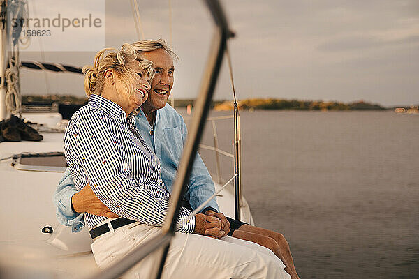 Glückliche Senior Paar sitzt auf dem Rand des Segelbootes während des Sonnenuntergangs