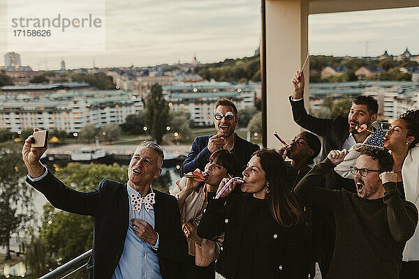 Fröhliche männliche und weibliche Kollegen nehmen Selfie auf Smartphone während der Party im Büro