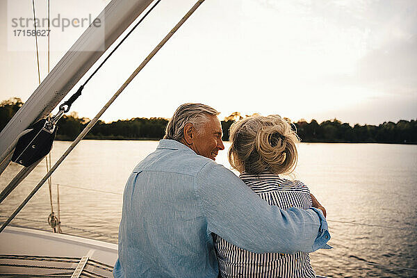 Senior Mann umarmt Frau beim Sitzen im Boot während des Sonnenuntergangs