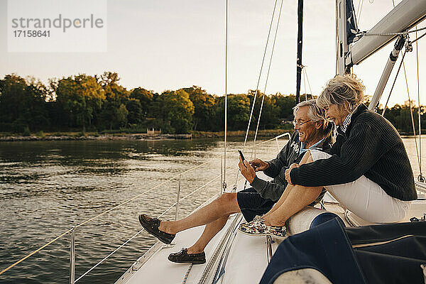 Glückliches älteres Paar  das während des Sonnenuntergangs ein Mobiltelefon benutzt