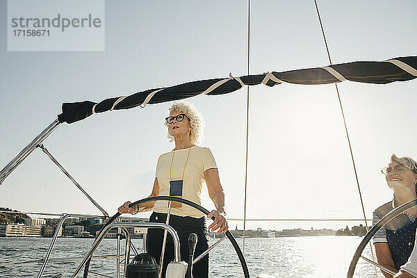 Senior Frau Segeln Boot mit weiblichen Freund gegen klaren Himmel am sonnigen Tag