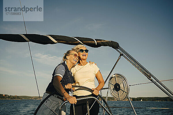 Fröhliche Freundinnen schauen weg  während sie in einem Boot gegen den Himmel stehen