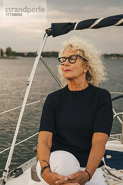 Senior Frau mit geschlossenen Augen sitzen auf Boot während des Sonnenuntergangs