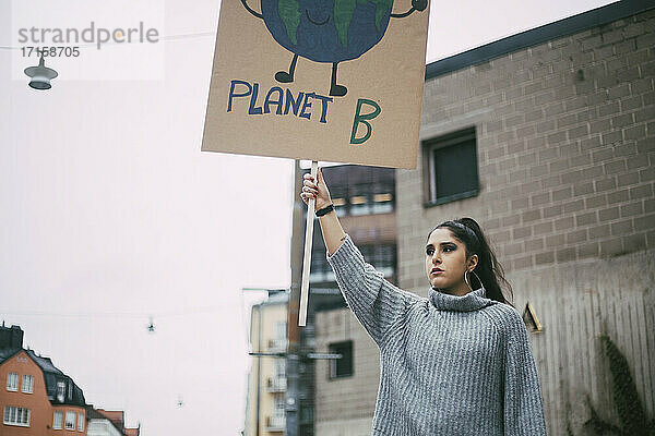 Weibliche Aktivistin schaut weg  während sie ein Planet-Earth-Poster während einer sozialen Bewegung hält