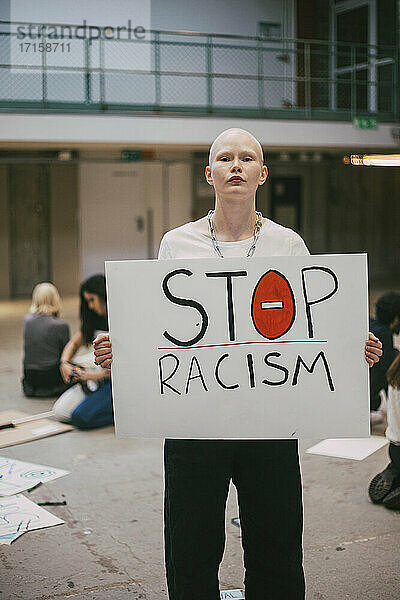 Junge weibliche Aktivistin mit Stop-Rassismus-Plakat im Gebäude stehend