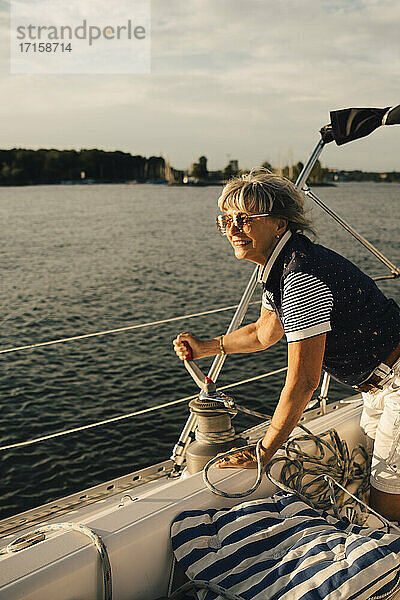 Lächelnde ältere Frau dreht Griff auf Boot im Meer während des sonnigen Tages