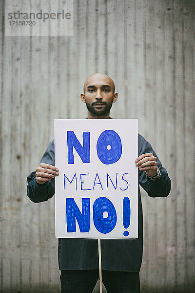 Porträt eines männlichen Aktivisten  der ein No means no -Plakat an eine Wand hält