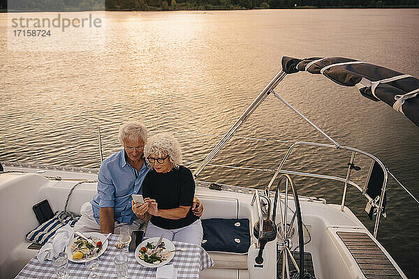 Hoher Winkel Ansicht der älteren Paar nehmen Selfie durch Handy in Segelboot während des Sonnenuntergangs