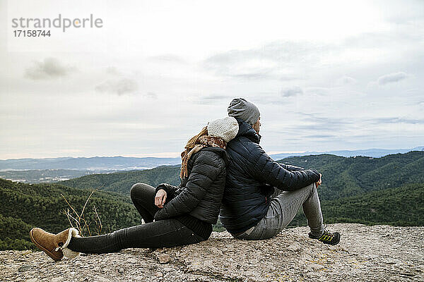 Paar sitzt Rücken an Rücken auf dem Aussichtspunkt gegen den Himmel
