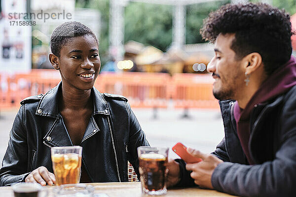 Smiling friends talking while sitting at sidewalk cafe