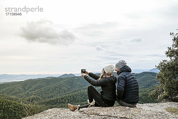 Paar  das ein Selfie macht  während es auf dem Beobachtungspunkt gegen den Himmel sitzt
