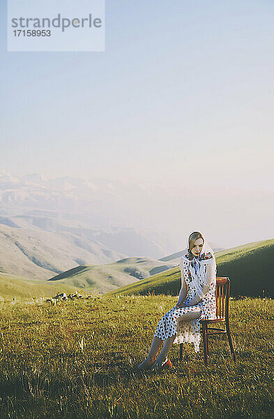 Woman with polka dot dress sitting at chair against clear sky