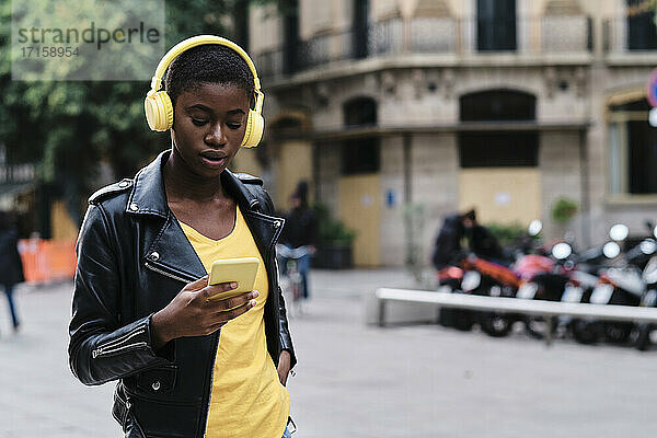Young woman wearing headphones using mobile phone while standing in city