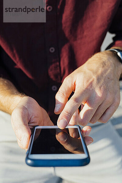 Geschäftsmann zeigt auf den Bildschirm seines Mobiltelefons  während er im Freien sitzt