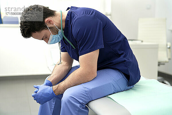 Exhausted male doctor with eyes closed sitting in medical clinic