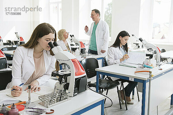 Forscher im weißen Kittel bei der Arbeit mit dem Mikroskop im naturwissenschaftlichen Unterricht