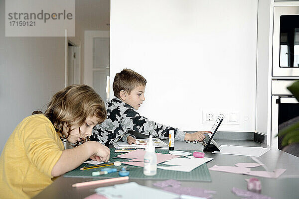 Siblings doing art and craft while using digital tablet at home