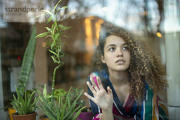 Nachdenkliche junge Frau durch Glasfenster zu Hause gesehen