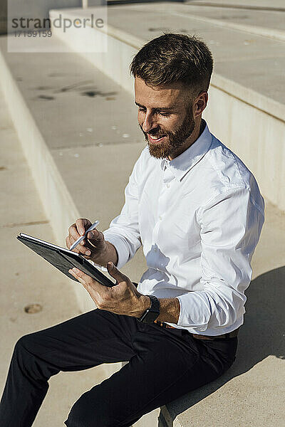 Smiling businessman using digital tablet while sitting on steps