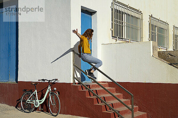Junge Frau rutscht auf dem Geländer von weißen gebaut Struktur während sonnigen Tag