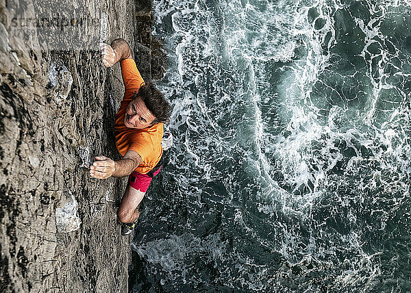 Leidenschaftlicher männlicher Felskletterer klettert an einer Felswand am Meer