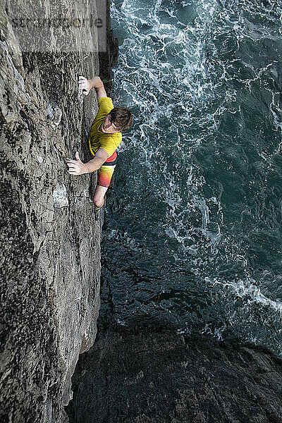 Abenteuerlustiger männlicher Felskletterer klettert auf eine Klippe über dem Meer