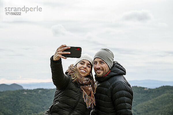 Lächelndes Touristenpaar macht ein Selfie gegen den Himmel im Winter
