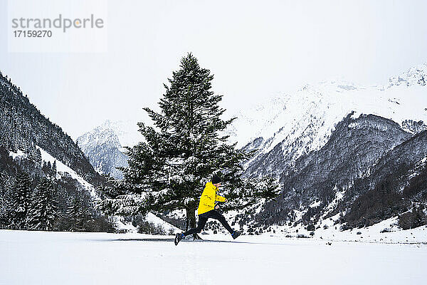 Man jumping by tree on snow covered valley