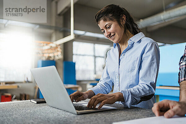 Smiling businesswoman working on laptop while standing by colleague at industry