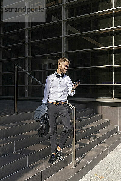 Mid adult businessman using mobile phone while standing on steps