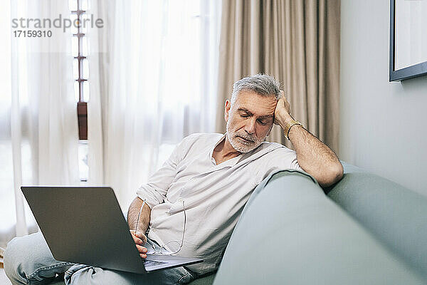 Exhausted man with laptop sitting on sofa in hotel room
